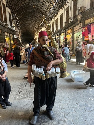 Traditional vendor in Damascene dress selling arq sus and tamarind juice from a large copper urn in the Al-Hamidiyah Souk, Damascus, Syria